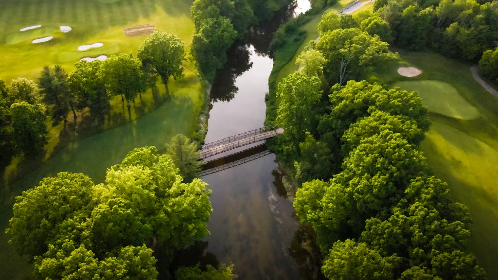 Aerial view of bridge. A river runs in the middle connecting two sides of the golf course.